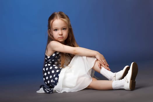 Adorable little blonde posing in smart dress, on blue background