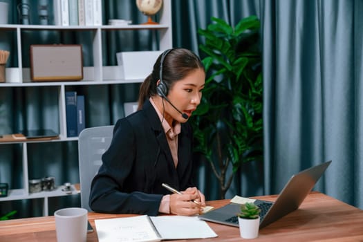 Asian call center with headset and microphone working on her laptop. Female operator provide exceptional customer service. Supportive call center agent helping customer on inquiry. Enthusiastic