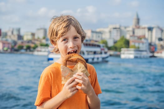 Boy in Istanbul having breakfast with Simit and a glass of Turkish tea. Glass of Turkish tea and bagel Simit against golden horn bay and the Galata Tower in Istanbul, Turkey. Turkiye. Traveling with kids concept.