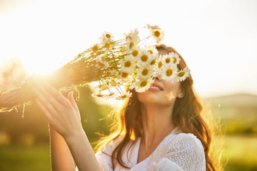 a girl in a light dress stands in nature in the sunset rays of the sun and covers her face with a bouquet of daisies. High quality photo