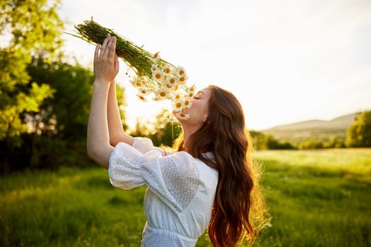 a girl in a light dress stands in nature in the sunset rays of the sun and covers her face with a bouquet of daisies. High quality photo