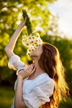 close portrait of a red-haired woman in a light dress sniffing a bouquet of daisies. nature, sunny weather. High quality photo