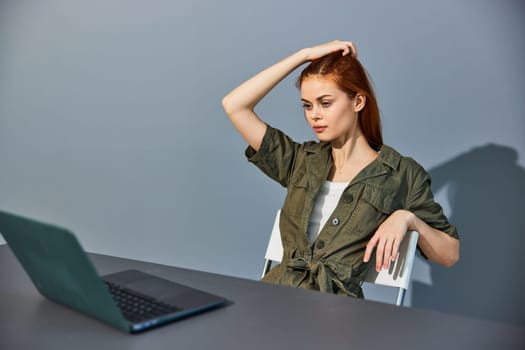 a serious, tired woman sits at work at a laptop in the office and straightens her hair with her hand. High quality photo