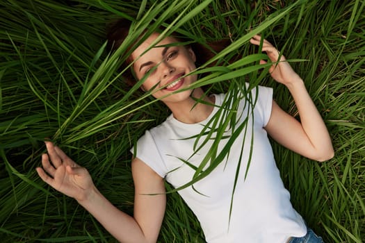 happy woman lies in high grass biting leaves with beautiful, even teeth. High quality photo