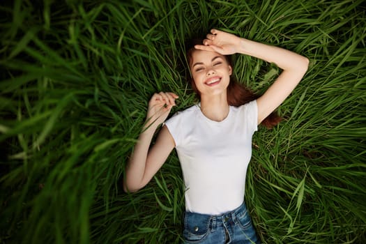 a portrait of a laughing woman with healthy, even teeth lies in the green grass. High quality photo