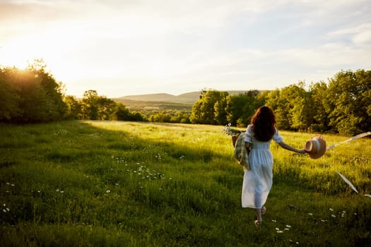 a woman in a light dress stands in a field during sunset with a wicker basket, a hat and a plaid in her hands. High quality photo