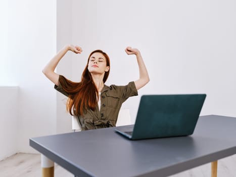 happy woman in winner pose sits at work desk with laptop and rejoices in her achievements. High quality photo