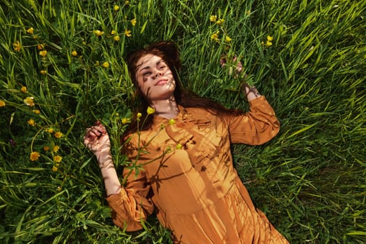 a calm woman with long red hair lies in a green field with yellow flowers, in an orange dress with her eyes closed, with a pleasant smile on her face, enjoying peace and recuperating. High quality photo