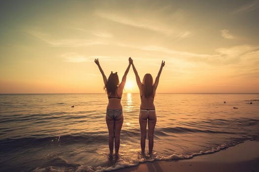 Happy Girls friends raising arms in the beach at sunset.