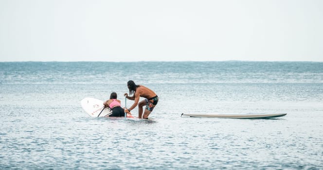Sea woman and man on sup. Silhouette of happy young woman and man, surfing on SUP board, confident paddling through water surface. Idyllic sunset. Active lifestyle at sea or river