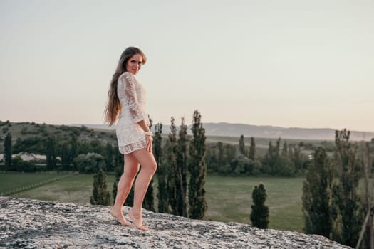 Romantic beautiful bride in white dress posing with sea and mountains in background. Stylish bride standing back on beautiful landscape of sea and mountains on sunset