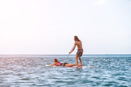 Sea woman and man on sup. Silhouette of happy young woman and man, surfing on SUP board, confident paddling through water surface. Idyllic sunset. Active lifestyle at sea or river