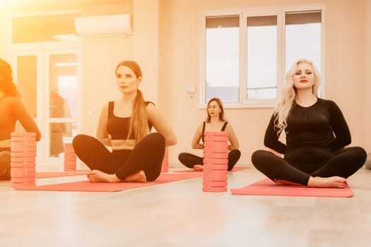 Group of young womans fitness instructor in Sportswear Leggings and Tops, stretching in the gym before pilates, on a yoga mat near the large window on a sunny day, female fitness yoga routine concept.