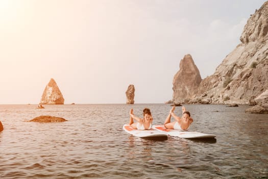 Woman sup yoga. Middle age sporty woman practising yoga pilates on paddle sup surfboard. Female stretching doing workout on sea water. Modern individual hipster outdoor summer sport activity