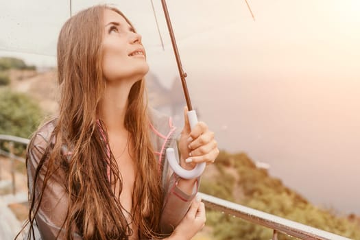 Woman rain park. Happy woman portrait wearing a raincoat with transparent umbrella outdoors on rainy day in park near sea. Girl on the nature on rainy overcast day