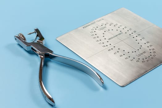 Dental hole punch and the metal plate on the blue background. Medical tools concept.