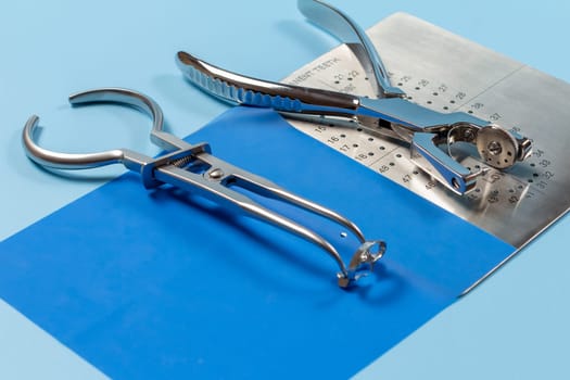 Dental hole punch, the metal plate, the rubber dam and the rubber dam forceps on the blue background. Top view. Medical tools concept.