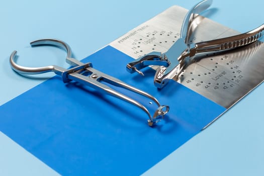 Dental hole punch, the metal plate, the rubber dam and the rubber dam forceps on the blue background. Medical tools concept. Top view.