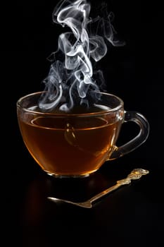 Glass cup of black tea with rising steam on the black background.