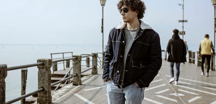 A young man taking a pensive walk along a pier, lost in his thoughts and seemingly carrying a heavy heart.