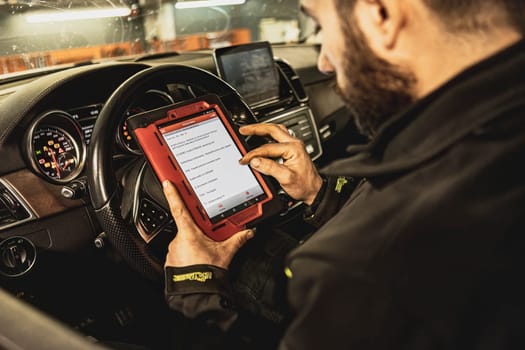 A mechanic's hands use a diagnostic tool to troubleshoot a modern car's computer system in a garage.