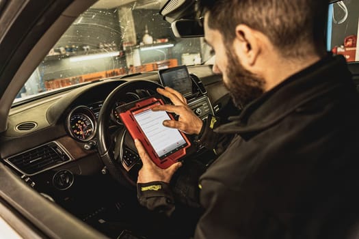 A mechanic's hands use a diagnostic tool to troubleshoot a modern car's computer system in a garage.