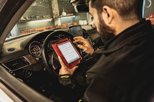 A mechanic's hands use a diagnostic tool to troubleshoot a modern car's computer system in a garage.