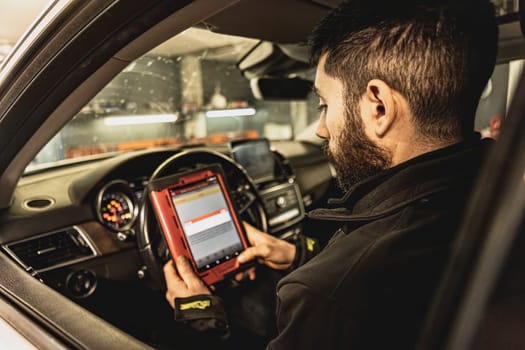 A mechanic's hands use a diagnostic tool to troubleshoot a modern car's computer system in a garage.