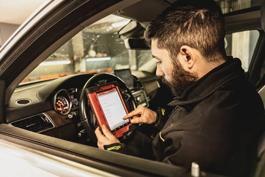 A mechanic's hands use a diagnostic tool to troubleshoot a modern car's computer system in a garage.