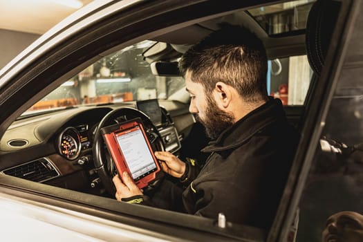 A mechanic's hands use a diagnostic tool to troubleshoot a modern car's computer system in a garage.