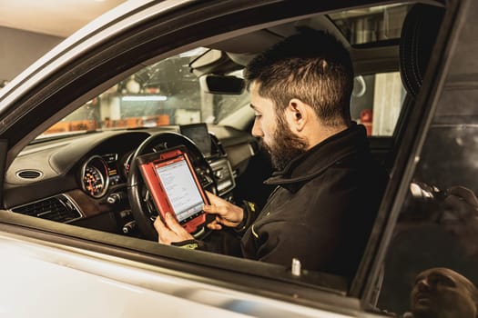 A mechanic's hands use a diagnostic tool to troubleshoot a modern car's computer system in a garage.