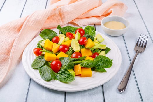 Fresh salad of avocado, mango, spinach and cherry tomatoes in a white plate on a wooden background. High quality photo