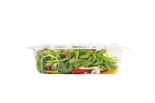 Fresh salad of cabbage, herbs, peppers, carrots and pomegranate seeds in a plastic container on a white background. High quality photo