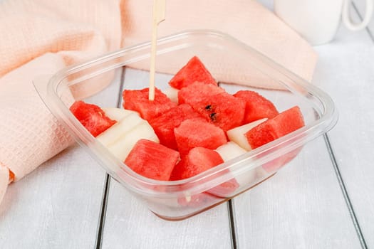 Fruit salad with watermelon and melon in a plastic container on a wooden background. High quality photo