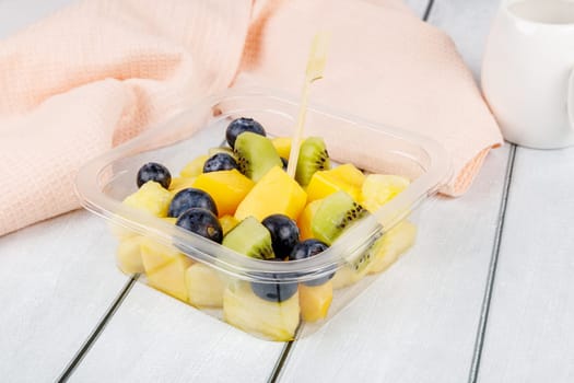 Fruit salad of pineapple, mango, kiwi and blueberries in a plastic container on a wooden background. High quality photo