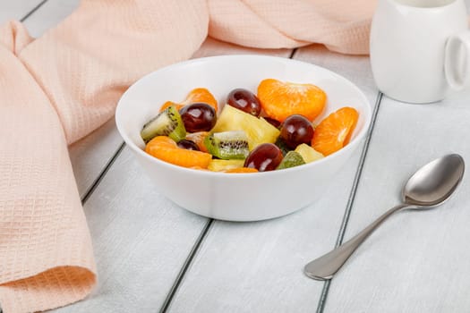 Fruit salad of pineapple, orange, kiwi and grapes in a plate on a wooden background. High quality photo