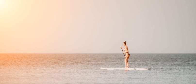 Sea woman sup. Silhouette of happy middle aged woman in rainbow bikini, surfing on SUP board, confident paddling through water surface. Idyllic sunset. Active lifestyle at sea or river