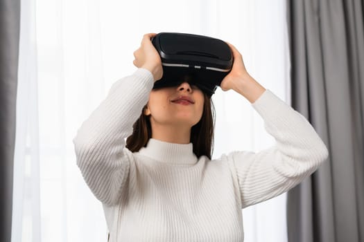 Amazed young girl in virtual reality using VR glasses headset explores metaverse in the living room