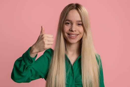 Like. Caucasian young woman in dress raises thumbs up agrees with something, gives positive reply recommends advertisement likes good. Pretty teen girl isolated alone on pink studio background