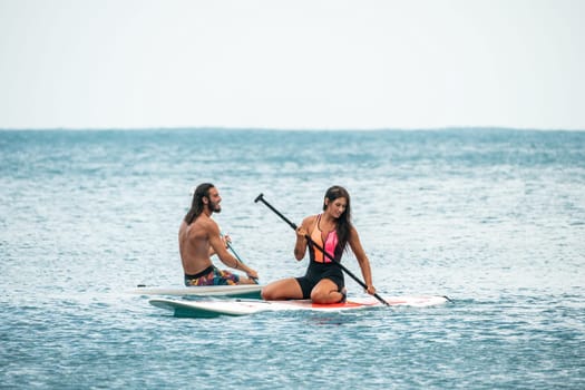 Sea woman and man on sup. Silhouette of happy young woman and man, surfing on SUP board, confident paddling through water surface. Idyllic sunset. Active lifestyle at sea or river