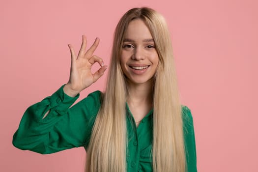 Okay. Joyful happy caucasian woman looking approvingly at camera showing approve feedback gesture like Ok sign positive something good. Pretty smiling girl on pink background. People sincere emotion