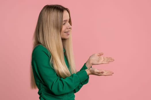 Caucasian woman showing thumbs up and pointing empty right place, advertising area for commercial text, banner, logo, copy space for goods promotion. Young teen girl isolated on pink studio background
