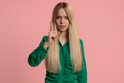 Caucasian pretty woman shakes finger and saying No, be careful, scolding, giving advice to avoid danger mistake, disapproval sign. Young girl isolated on pink studio background. People lifestyles