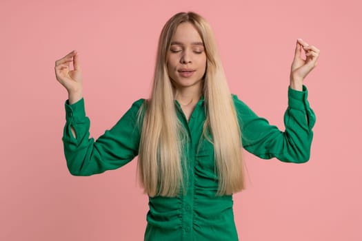 Keep calm down, relax, inner balance. Young caucasian woman breathes deeply with mudra gesture, eyes closed, meditating with concentrated thoughts, peaceful mind. Girl isolated on pink background