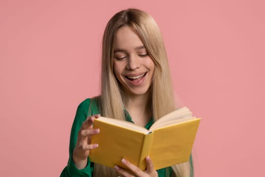 Happy caucasian woman reading funny interesting fairytale story book, leisure hobby, knowledge wisdom, education, learning, study, wow. Pretty smiling teen girl isolated on pink studio background