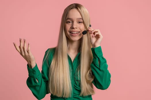 Young woman wearing headset, freelance worker, call center or support service operator helpline, having talk with client or colleague, communication support. Teenager girl isolated on pink background