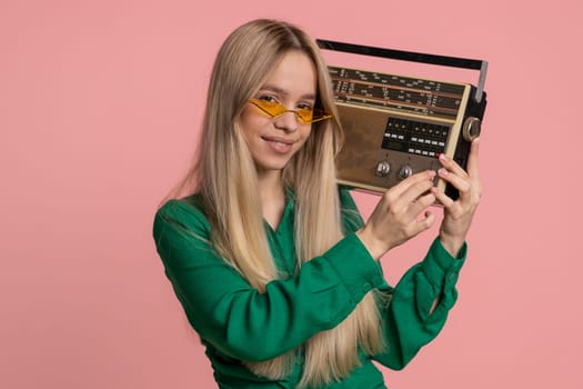 Happy Caucasian woman using retro tape record player to listen music, disco dancing of favorite track, having fun, entertaining, fan of vintage technologies. Pretty girl isolated on pink background