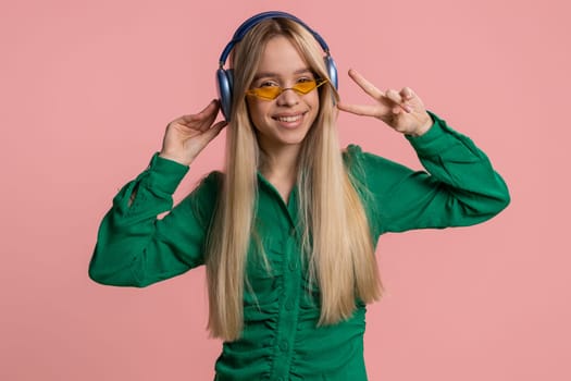 Pretty woman in headphones listening music, smiling dancing disco party, music rhythmically moving her hands, having fun, celebrating success winning, birthday. Teenager girl kid on pink background