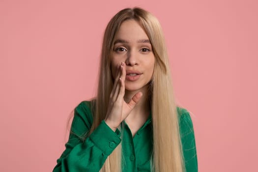 Keep my secrets, silence. Young woman whisper news rumors holding hands near mouth, share gossip, quiet. Teenager child girl telling interesting confidential story isolated on pink background, indoors