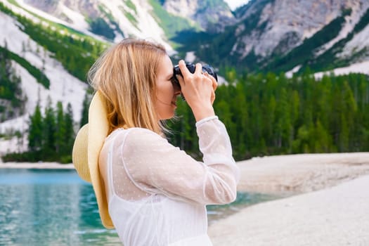 Young woman photographer holding a camera and taking photos of the Alps. A girl in a white dress and hat enjoying view of mountains.